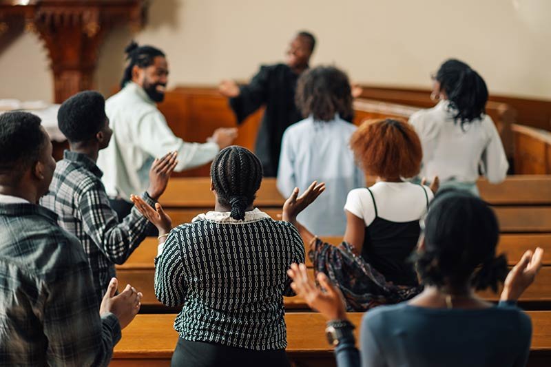 A group of Black congregants are standing and worshipping in a church sanctuary.